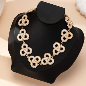 Dettaglio collana vintage dorata con ciondoli in smalto bianco su un manichino nero
