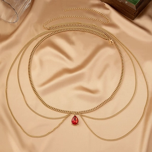 Detail of a layered gold waist chain featuring a red teardrop gemstone on silk fabric