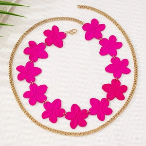 Détail de la chaîne à fleurs rose mat avec maillons dorés sur fond texturé fin