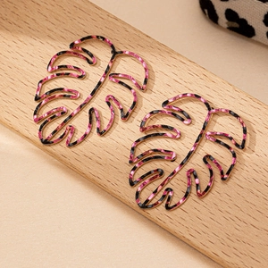 Gouden Monstera oorbellen met roze en zwarte luipaardprint op houten standaard