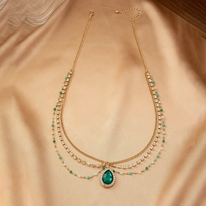 Détail d'un collier bohème doré avec une pierre verte en forme de goutte et des strass