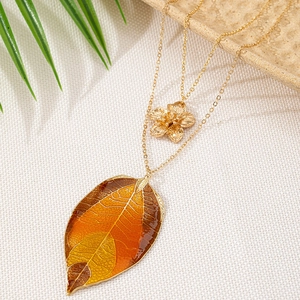 Double-layered gold necklace featuring a floral pendant and a gradient enamel leaf charm
