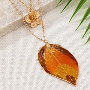 Double-layered gold necklace with metal flower and orange enamel leaf pendants