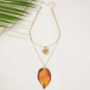 Detailed close-up of double-layer necklace with floral pendant and orange leaf on white fabric
