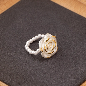 Detail view of pearl chain ring with a white rose and golden edges on a grey surface