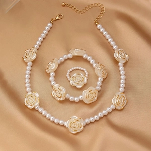 Elegantes Schmuckset mit weißen Perlen und Harzrosen auf champagnerfarbenem Seidenhintergrund