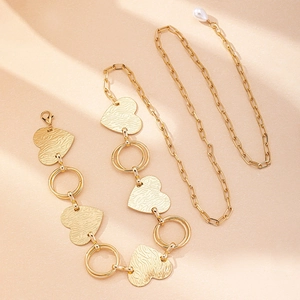 Chaîne de taille dorée avec maillons en cœur et pendentif perle sur fond beige