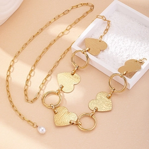 Chaîne de taille dorée avec pendentifs en cœur texturés et perle blanche sur fond orange clair