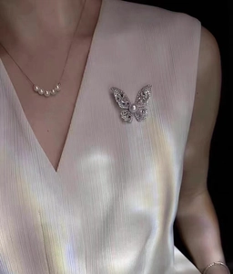 Detail einer funkelnden Schmetterlingsbrosche mit Perlen auf einer Plissee-Seidenbluse