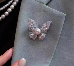 Detailansicht einer Schmetterlingsbrosche mit Kristallen und Perle am grauen Revers
