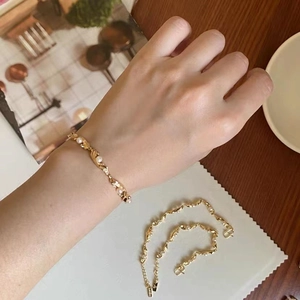 Detail of vintage gold leaf bracelet with white pearls shown on a model wrist and fabric