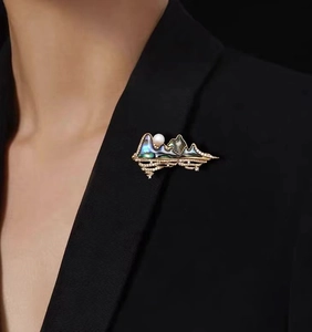 Detailed view of 18K gold plated mountain brooch with shell inlay and pearl on black suit