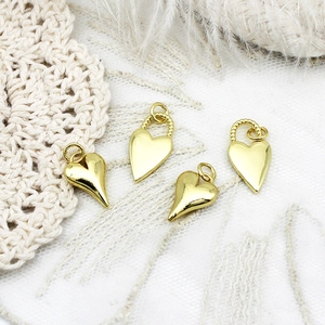Polished 18K gold heart charms with twisted loop details on white lace and feather background