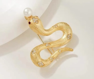 Détail d'une broche serpent dorée avec écailles texturées perles blanches et yeux rouges