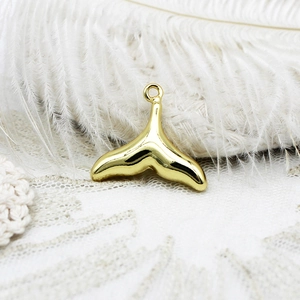 Detailed view of an 18K gold-plated whale tail pendant on white lace and feather background