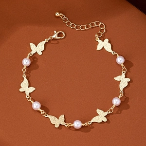 Detailaufnahme goldene Fußkette mit matten Schmetterlingen und Perlen auf dunklem Grund