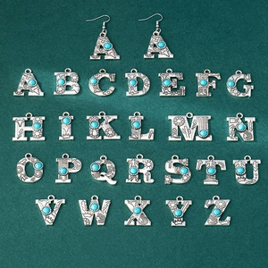 Detail of vintage silver alphabet pendants with turquoise inlay and western floral carvings