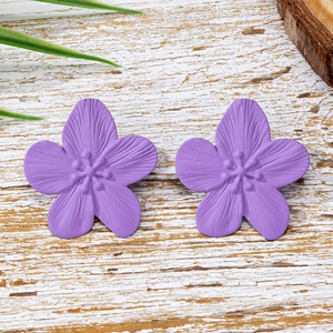 Elegantes pendientes de flor púrpura de cinco pétalos con textura mate en fondo madera