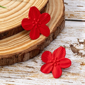 Detalle de pendientes de flor roja de cinco pétalos con acabado mate sobre base de madera