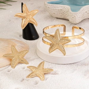 Three-piece golden starfish jewelry set with textured bracelet and ring on white sand beach