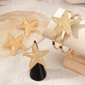 Golden starfish jewelry set including open bracelet, ring and clips on a beach setting