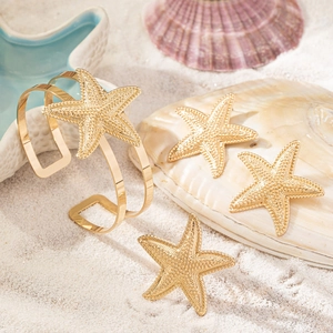 Detailed macro view of gold starfish bracelet and earrings on white beach sand