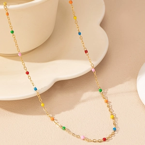 Minimalist gold chain necklace with colorful enamel beads on a warm aesthetic setting