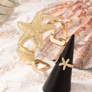 Set di gioielli dorati a tema oceano con stelle marine e conchiglie su sfondo sabbia