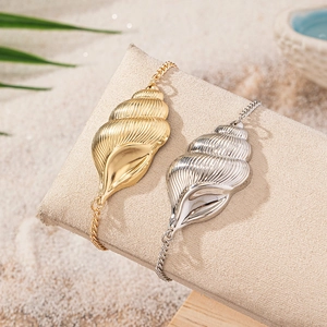 Golden and silver conch shell anklets on sandy beach display with tropical palm leaf