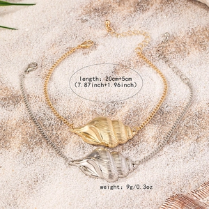 Detailed view of conch shell charm anklets in gold and silver on white beach sand background