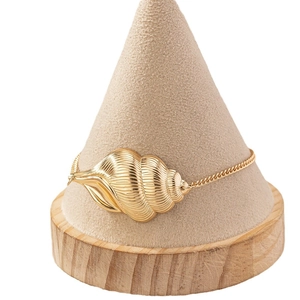 Golden conch shell charm anklet with delicate spiral texture on minimalist jewelry stand