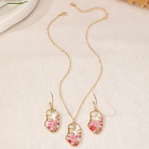 Detailopname van goudkleurige sieradenset met gezichtsvorm en roze gedroogde bloemen