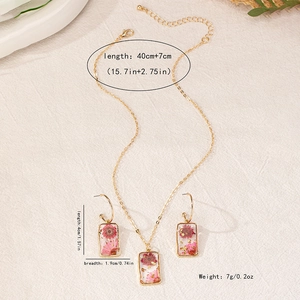 Detail van gouden ketting en oorbellen set met echte roze droogbloemen in hars