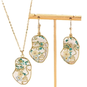 Elegante goudkleurige sieradenset met abstracte gezichten en gedroogde bloemen