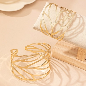 Bracciali rigidi aperti dorati con motivo a foglia su un supporto per gioielli in legno