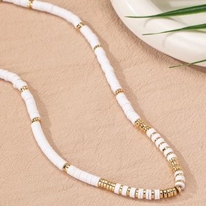 Collar minimalista de discos de arcilla blanca con espaciadores dorados sobre tela texturizada