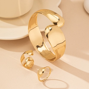 Set di gioielli dorati con bracciale aperto e anelli regolabili dal design fluido