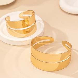 Dettaglio di due bracciali rigidi dorati a doppia fascia con design aperto su vassoio