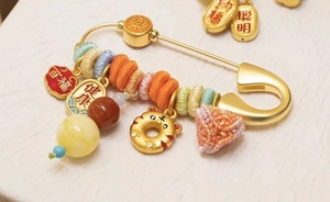 Macro detail of a golden baby safety pin with traditional Chinese charms and tiger pendant