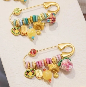 Macro detail of gold safety pin brooches featuring woven beads and traditional pendants