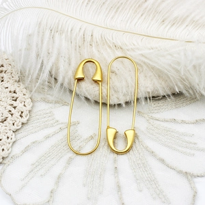 Matte gold safety pin earrings set against white feathers and crochet lace texture