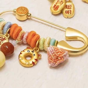 Traditional gold safety pin brooch with colorful beads, zodiac tiger, and lucky charms