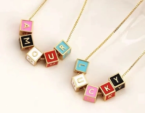 Détail de perles émaillées colorées épelant AMOUR et LUCKY sur des colliers dorés