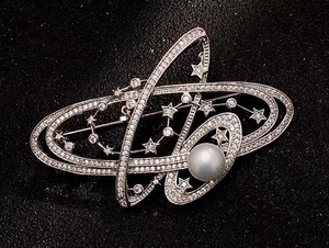 Macro shot of silver galaxy brooch featuring micro-pave crystals and a large pearl
