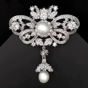 Close-up of luxury silver bow brooch with micro-pave zircons and water-drop pearl pendant