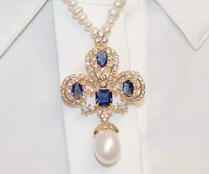 Macro detail of royal fleur-de-lis brooch featuring blue sapphire and teardrop pearl