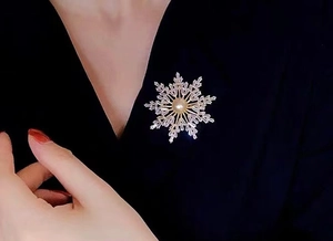 Detailed view of a gold snowflake brooch with a white pearl and cubic zirconia stones