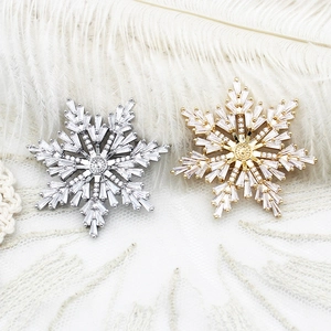 Elegant silver and gold snowflake brooches with cubic zirconia on white feather background
