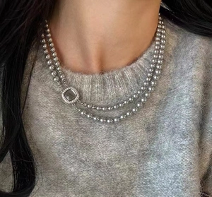 Detail of a grey double-layered pearl necklace with a square micro-pave clasp on a sweater