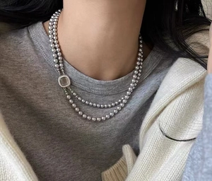 Detailed close-up of a double-layer pearl necklace with a square diamond buckle on a model